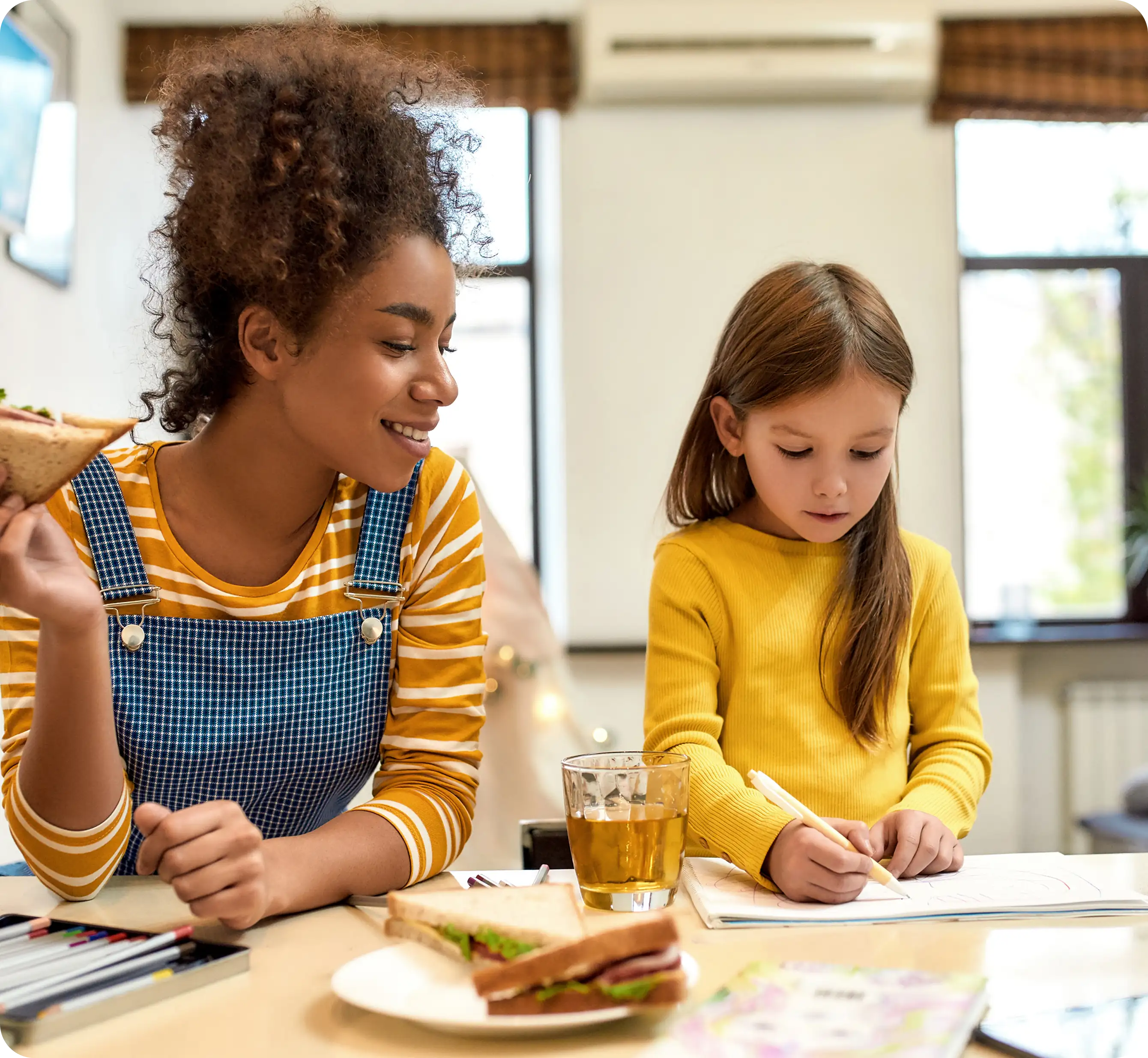 Woman helping girl with homework at table.